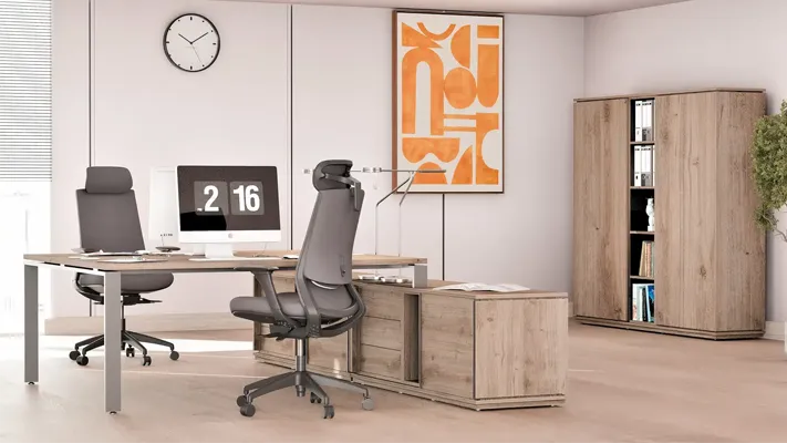 Zestaw mebli w biurze - biurko na komodzie, 2 zielone krzesła, szafa z półkami. Za oknem - park i osiedle mieszkaniowe.